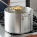 A person stirring a Choice aluminum sauce pot of pasta on a stove.