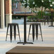 A Lancaster Table & Seating Excalibur square counter height table with a textured farmhouse finish and cross base plate with three stools on a patio.