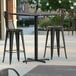 A Lancaster Table & Seating square bar height table with a black and white cross base plate on a patio.