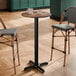 A round bar height table with a textured farmhouse finish and a black cross base plate.