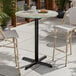 A round bar height table with a textured canyon painted faux metal finish and a black cross base plate.