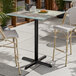 A square bar height table with a textured canyon painted faux metal finish and a black cross base plate.