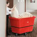 A woman using a Lavex red cube truck to hold a large white bag.