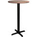 A round Lancaster Table & Seating bar height table with a wood top and black pole.