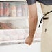 An aproned man reaching into a white Avantco air curtain merchandiser.