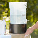 A person washing their hands in a white round beverage dispenser with a black base.