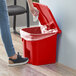 A person using a red Lavex step-on trash can to throw a white cloth into it.