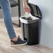 A hand putting a white bag in a Lavex black rectangular step-on trash can.