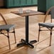 A square standard height table with a textured farmhouse finish and a black cross base plate, accompanied by two chairs.