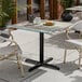 A square standard height table with a textured canyon painted faux metal finish and a black cross base plate.