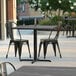 A Lancaster Table & Seating square dining table with a cross base on an outdoor patio.