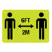 A yellow rectangular sign with black figures of two people and text reading "Please Practice Social Distancing" and "6 Ft. / 2 M"