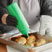 A person in a black glove using a Choice green wide mouth squeeze bottle to pour sauce on food.