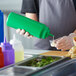 A person pouring sauce from a green Choice Wide Mouth Squeeze Bottle into a small cup.