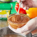 A gloved hand holding a bowl of liquid with a spoon.