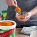 A person mixing Knorr Caldo de Tomate con sabor de Pollo into food in a bowl.