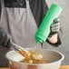 A person in gloves using a green Choice wide mouth squeeze bottle to pour sauce on a bowl of food.