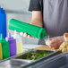 A person pouring sauce from a green Choice squeeze bottle into a small cup.