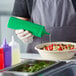 A hand holding a green Choice wide mouth squeeze bottle pouring sauce into a bowl of food.