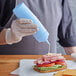 A person in gloves using a light blue Choice wide mouth squeeze bottle to pour mayo on a sandwich.