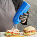 A person in black gloves and apron holding a Choice blue wide mouth squeeze bottle over a sandwich with meat and vegetables.