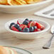 A Tuxton Reno eggshell china fruit bowl filled with fruit on a table.