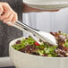 A person using Acopa 18/8 Stainless Steel Tongs to serve salad.