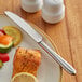 A plate of food with an Acopa Remy stainless steel dinner knife and a fork next to salmon.