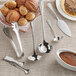 An Acopa stainless steel ladle next to a bowl of chocolate sauce.