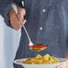 A person using an Acopa Industry stainless steel serving ladle to spoon pasta onto a plate.