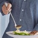 A person using an Acopa stainless steel serving ladle to spoon food onto a plate.