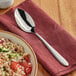 A white bowl of food with an Acopa Remy stainless steel serving spoon on a table.