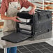 A woman in an apron using a Vesture heavy-duty thermal chafer pan carrier bag to put a metal tray in.