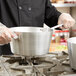 A person in a black uniform using a Vollrath Wear-Ever sauce pan over a stove.