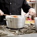 A chef in a black uniform stirring a Vollrath sauce pan on a stove.