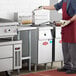 A man in a red apron using an Avantco electric floor fryer to cook food in a school kitchen.