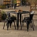 A Lancaster Table & Seating Onyx Black metal table with four black chairs outside.