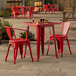 A Lancaster Table & Seating ruby red metal table and chairs on a stone patio.