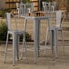 A Lancaster Table & Seating outdoor table with 2 gray metal bar stools.