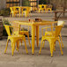 A Lancaster Table & Seating citrine yellow table and 4 chairs outside on a patio.