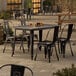 A Lancaster Table & Seating Alloy Series distressed onyx black standard height outdoor table with chairs on a patio.