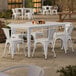 A Lancaster Table & Seating pearl white table with chairs on a outdoor patio.