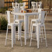 A Lancaster Table & Seating Pearl White bar height outdoor table with 4 white chairs on a patio.