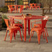 A Lancaster Table & Seating orange metal table and chairs on an outdoor patio.