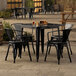 A Lancaster Table & Seating black metal table with four black chairs on an outdoor stone patio.