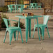 A Lancaster Table & Seating outdoor table in aquamarine with green chairs on a concrete patio.