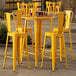 A Lancaster Table & Seating citrine yellow bar height table with chairs on an outdoor patio.