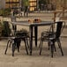 A Lancaster Table & Seating Alloy Series distressed onyx black metal table with four chairs on an outdoor patio.