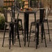 A Lancaster Table & Seating black bar height outdoor table with 4 black chairs.