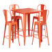 A Lancaster Table & Seating amber orange metal bar table with four chairs around it.